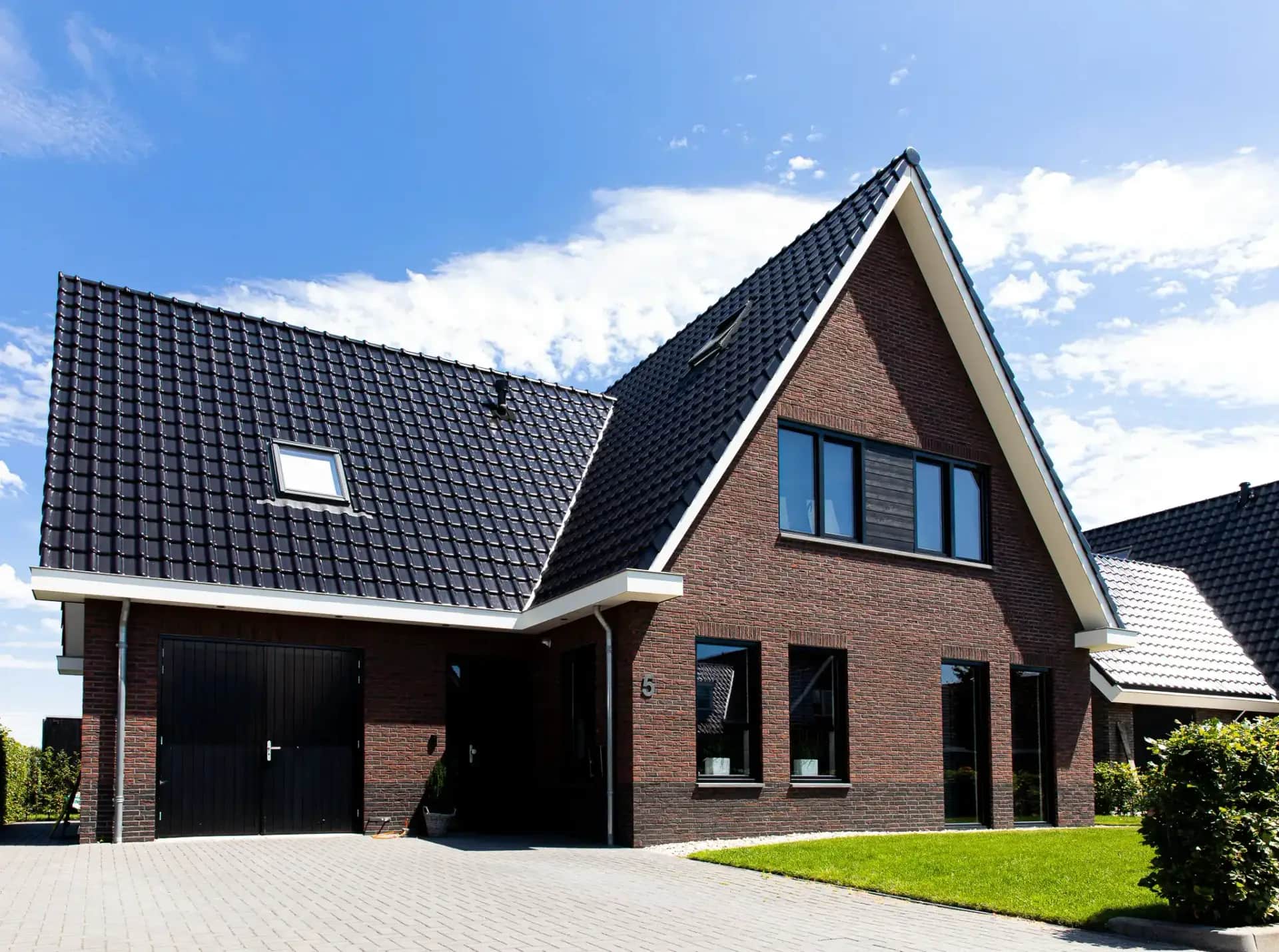 Traditionele T-kapwoning in Wolvega met bakstenen gevel, zwart dak, grote raampartijen en carport, gezien vanaf de voortuin