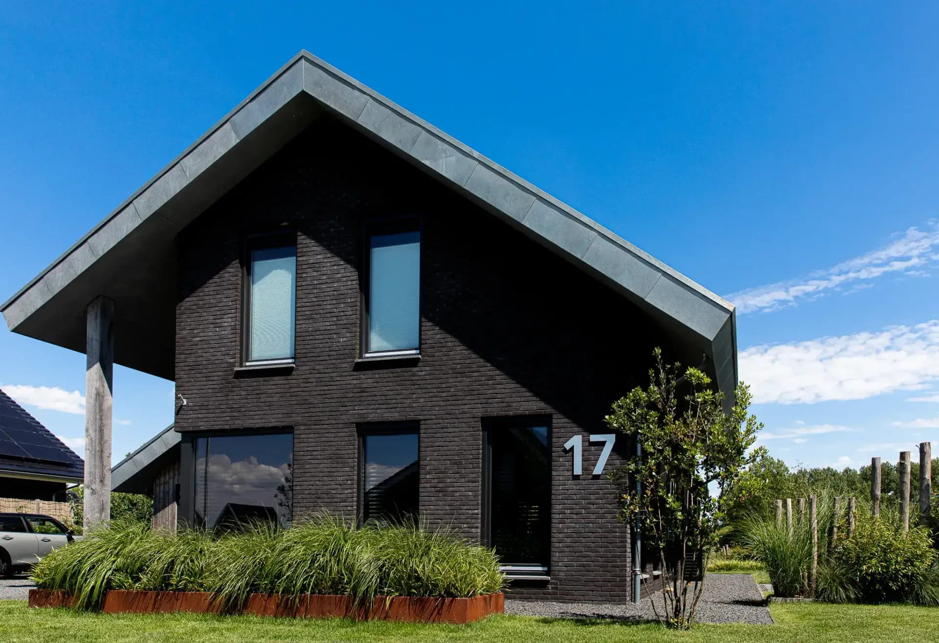 Minimalistische eigentijdse woning in Wolvega met overhangend asymmetrisch dak, hoekkozijnen, donker metselwerk, vergrijzend hout en zinken dakrand.