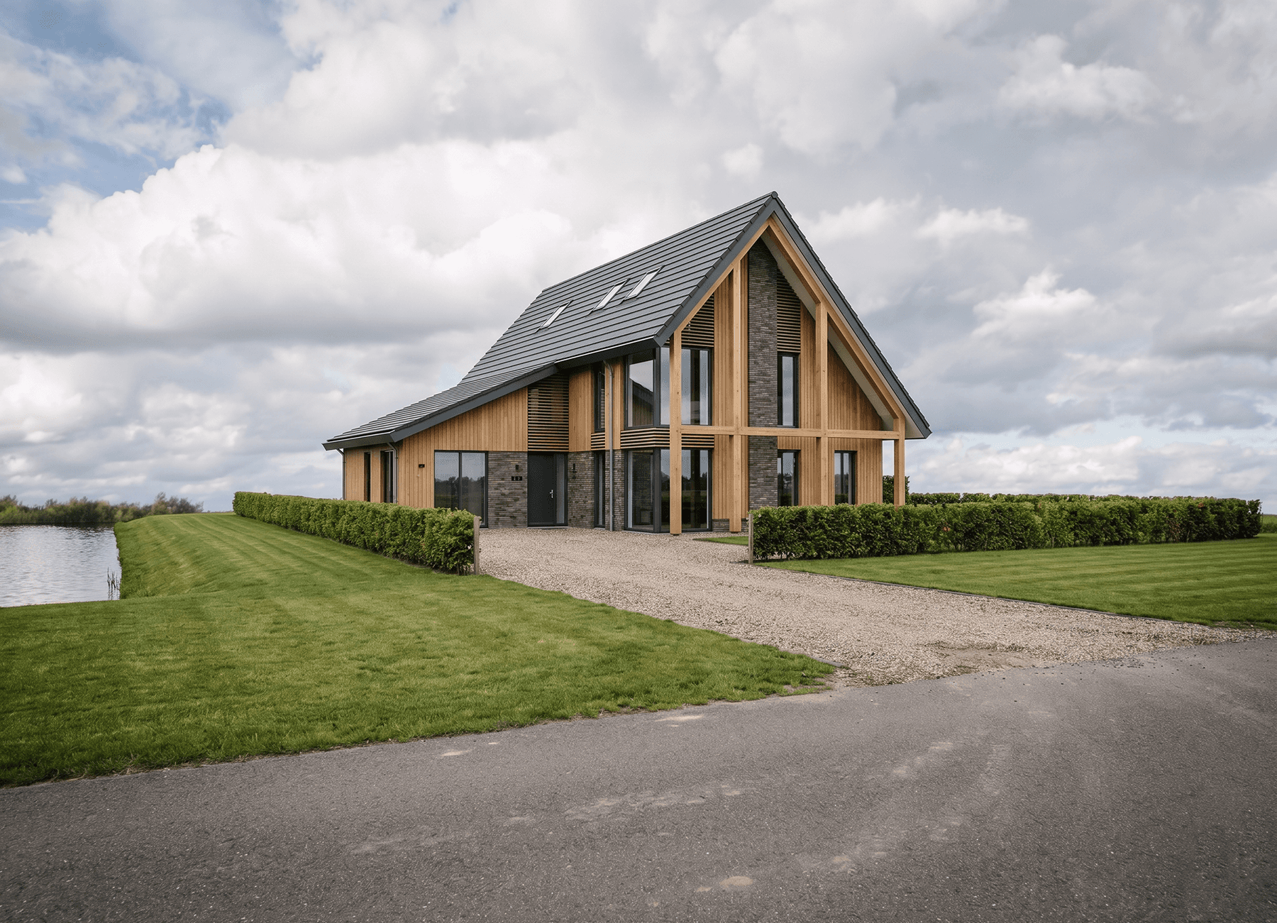 Schuurwoning in Wolvega met houten spanten, verticale houtbekleding, donker metselwerk en grote glaspartijen aan het water. Ontwerp door MArchitecten.