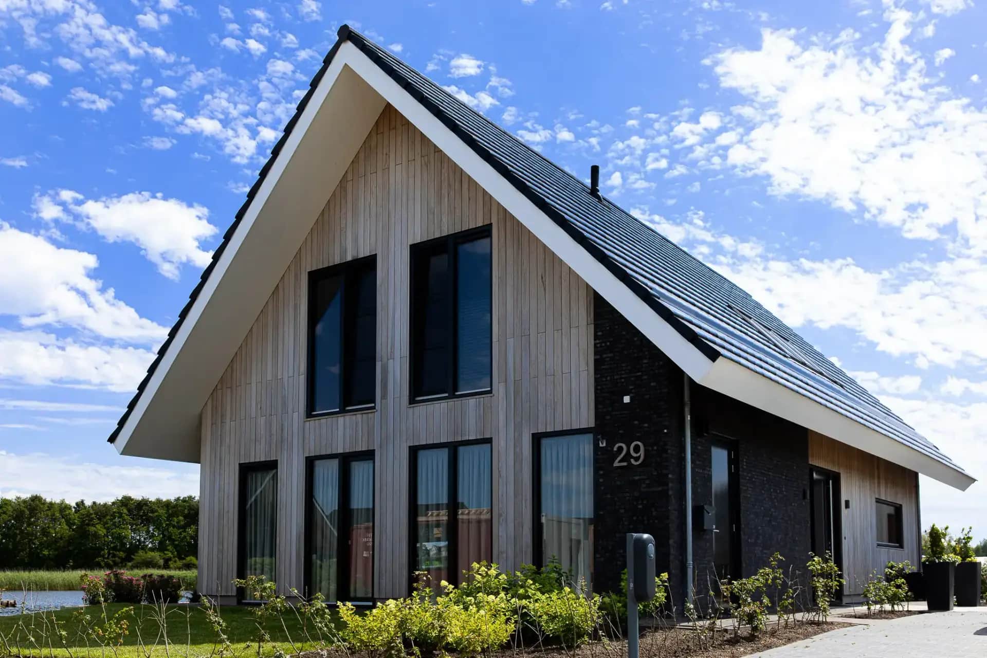 Moderne schuurwoning in Wolvega met hellend dak, grijze houten gevel, grote raampartijen en zwarte accenten, staand in landelijk gebied