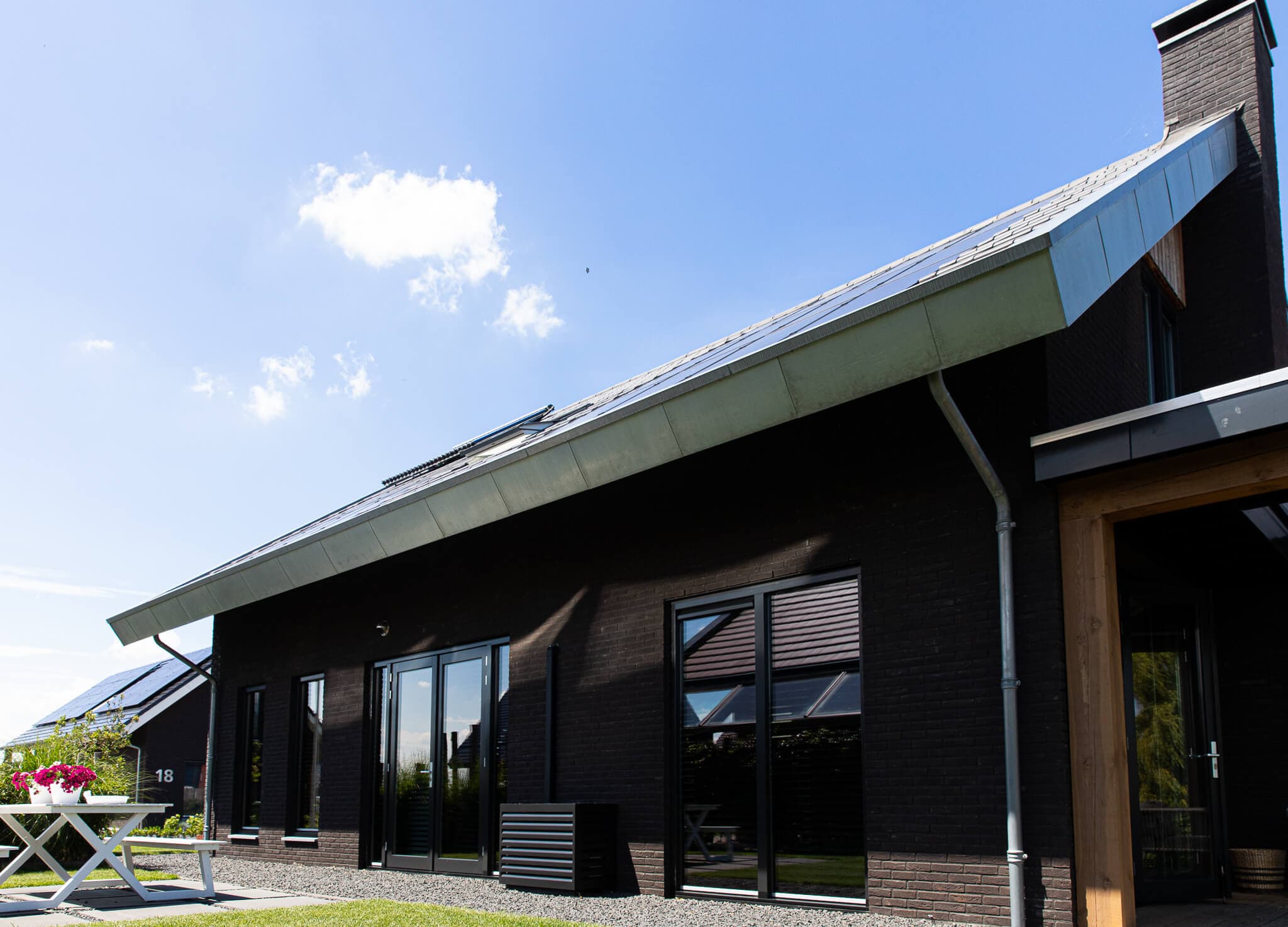 Minimalistische eigentijdse woning in Wolvega met overhangend asymmetrisch dak, hoekkozijnen, donker metselwerk, vergrijzend hout en zinken dakrand.