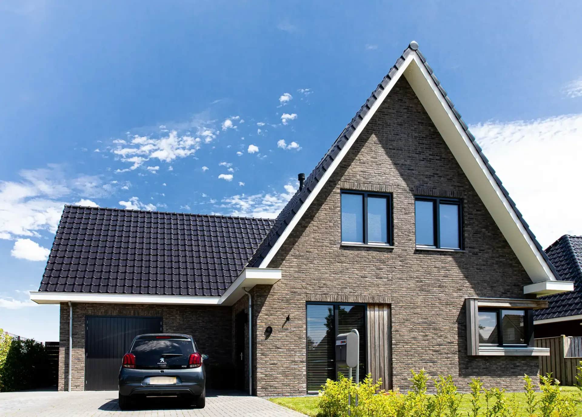Voorgevel van traditioneel woonhuis Argusvlinder in Wolvega met bakstenen gevel, schuine daken, grote ramen en oprit met auto