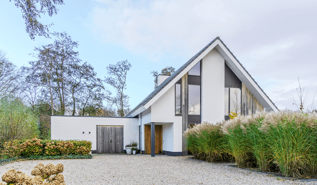 Modern wit woonhuis in Oranjewoud met karakteristieke gevelopbouw, grote raampartijen en grijsdak, omgeven door grind en siergrassen