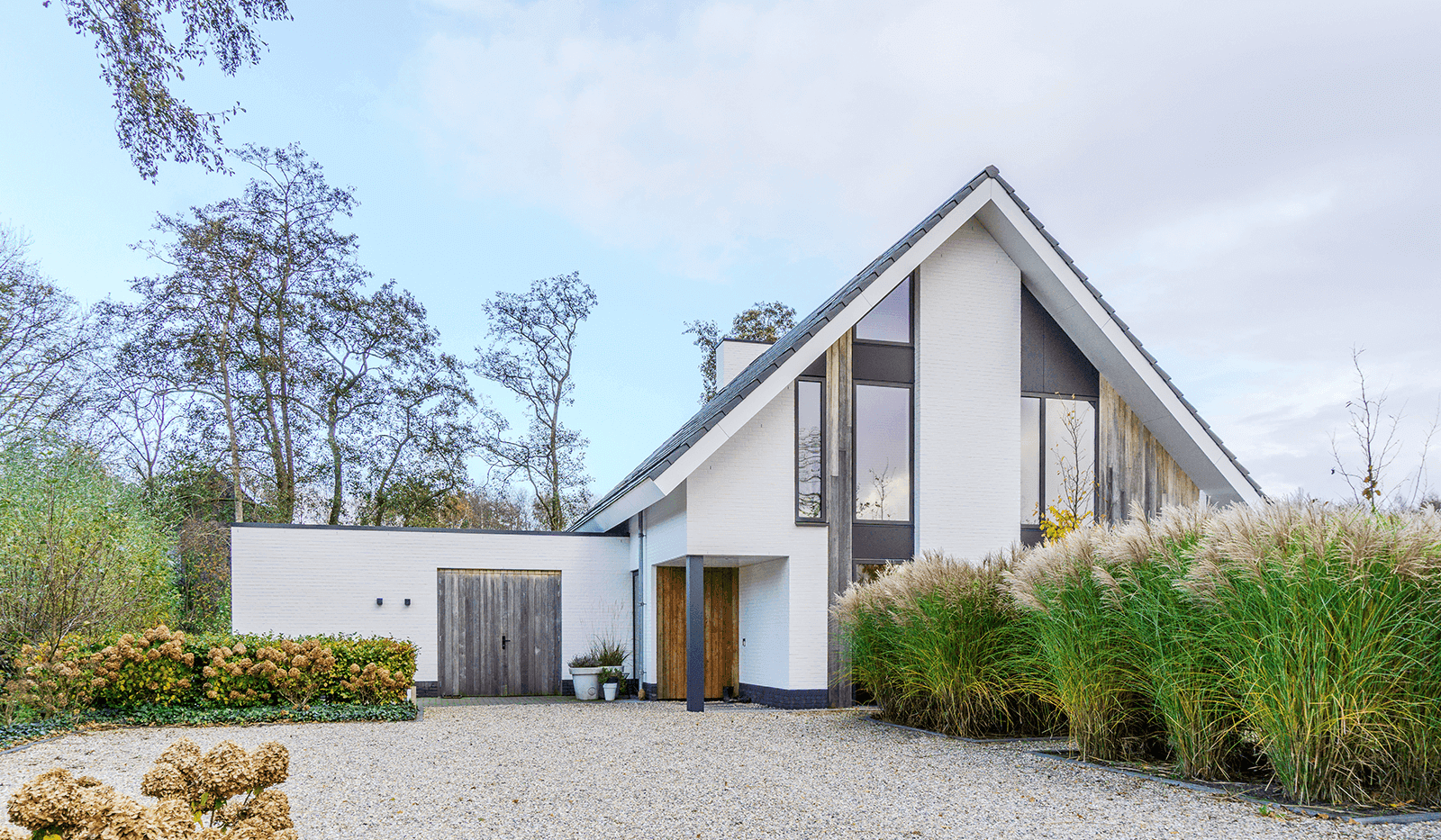 Modern wit woonhuis in Oranjewoud met karakteristieke gevelopbouw, grote raampartijen en grijsdak, omgeven door grind en siergrassen