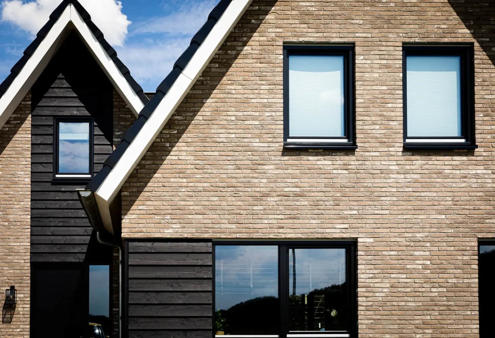 Moderne woning met dubbele kap in Willemsoord, bakstenen gevel met zwart houten dakkapel en grote raampartijen tegen blauwe lucht