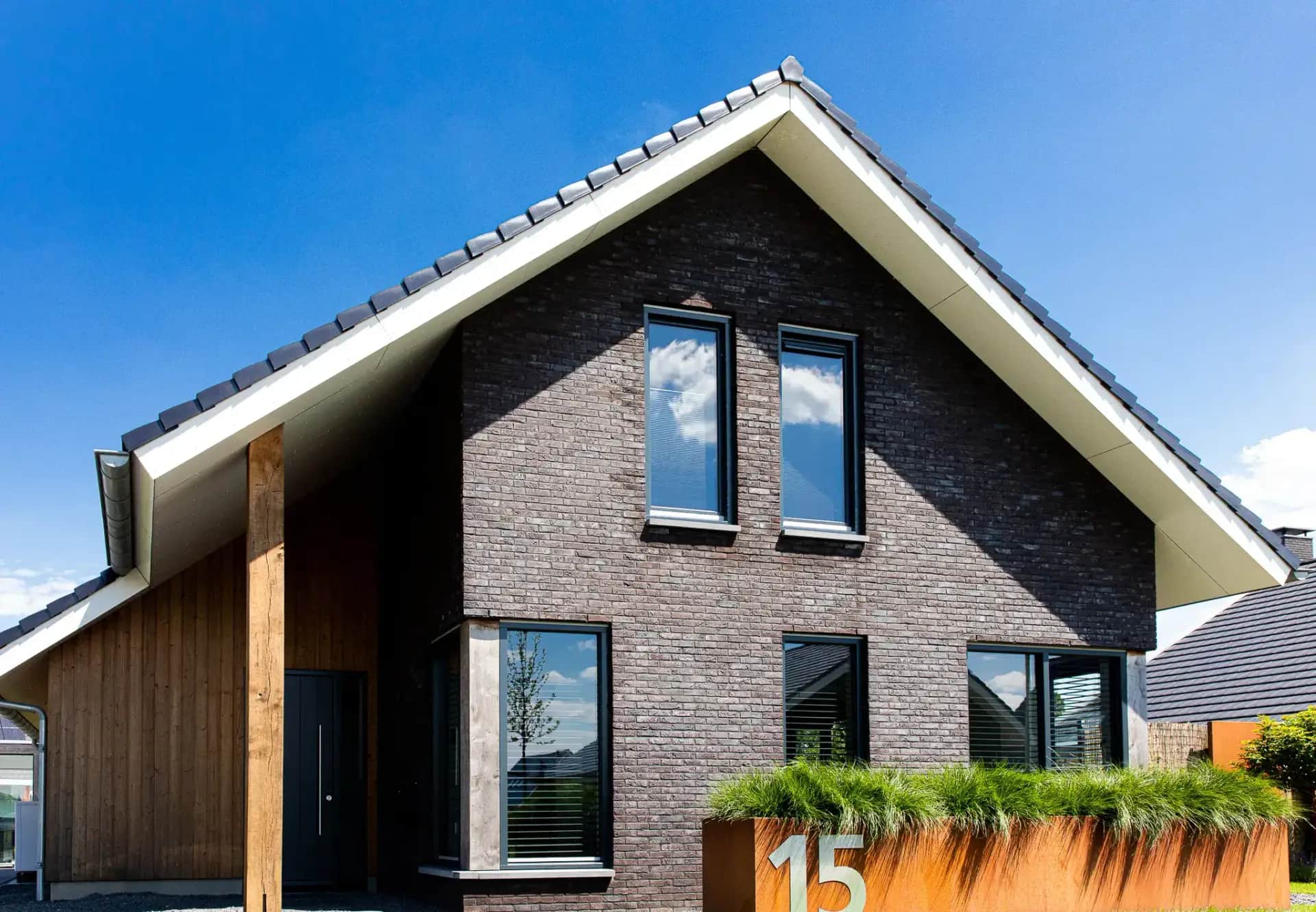 Modern woonhuis Heideblauwtje in Wolvega: voorgevel met donkere bakstenen, witte spouwmuur, grote raampartijen en houten accent aan zijkant