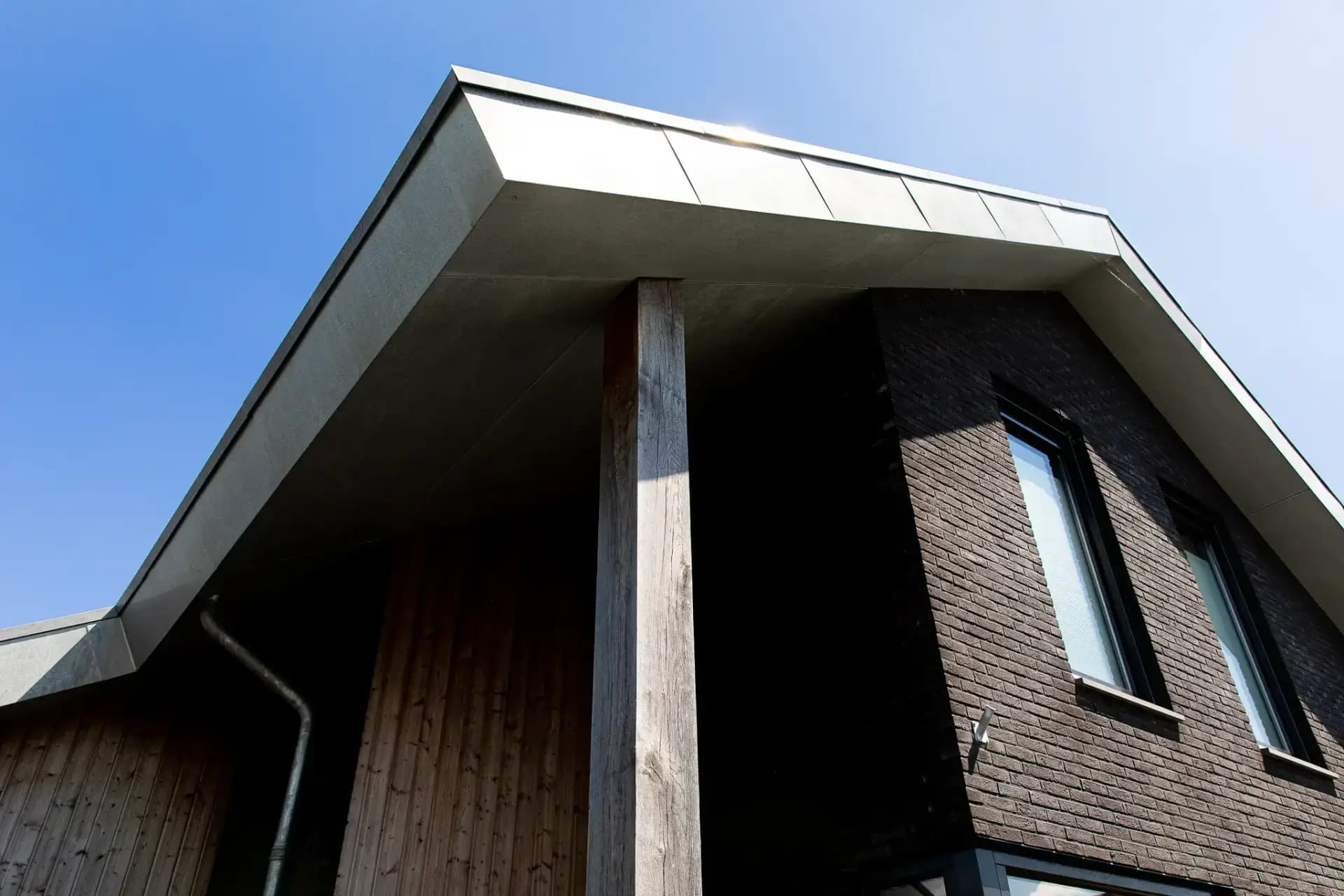 Minimalistische eigentijdse woning in Wolvega met overhangend asymmetrisch dak, hoekkozijnen, donker metselwerk, vergrijzend hout en zinken dakrand.